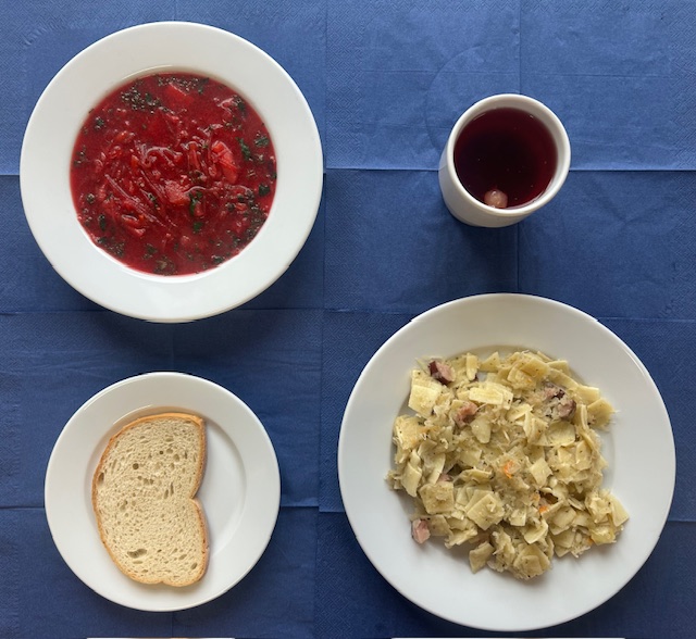 na talerzach barszcz czerwony, chleb zwykły pszenny, łazanki z kapustą, w kubku kompot