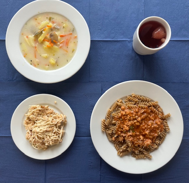 na talerzach zupa pieczarkowa, makaron razowy, sos boloński, surówka z selera i jabłka, w kubku kompot