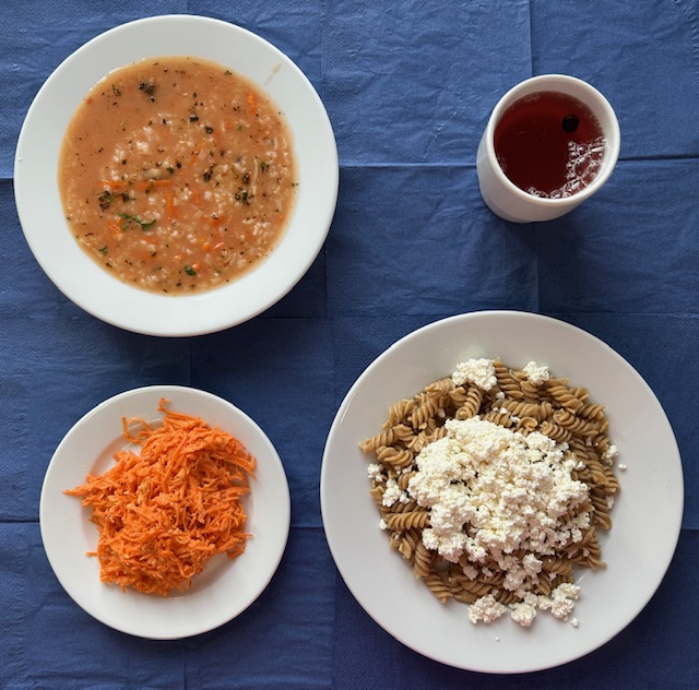 na talerzach zupa pomidorowa z ryżem, makaron razowy z serem, surówka z marchwi, chrzanu i słonecznika, w kubku kompot