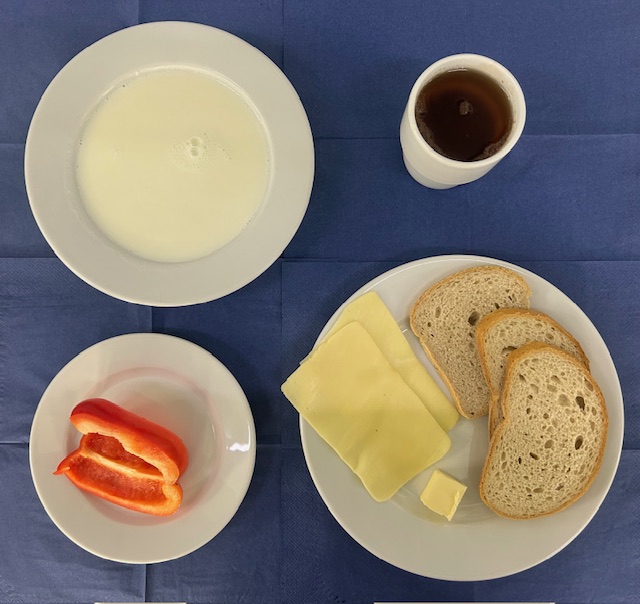 na talerzach kasza jaglana na mleku, chleb pszenny, chleb sitkowy, masło, ser żółty gouda, w kubku herbata z  cytryną