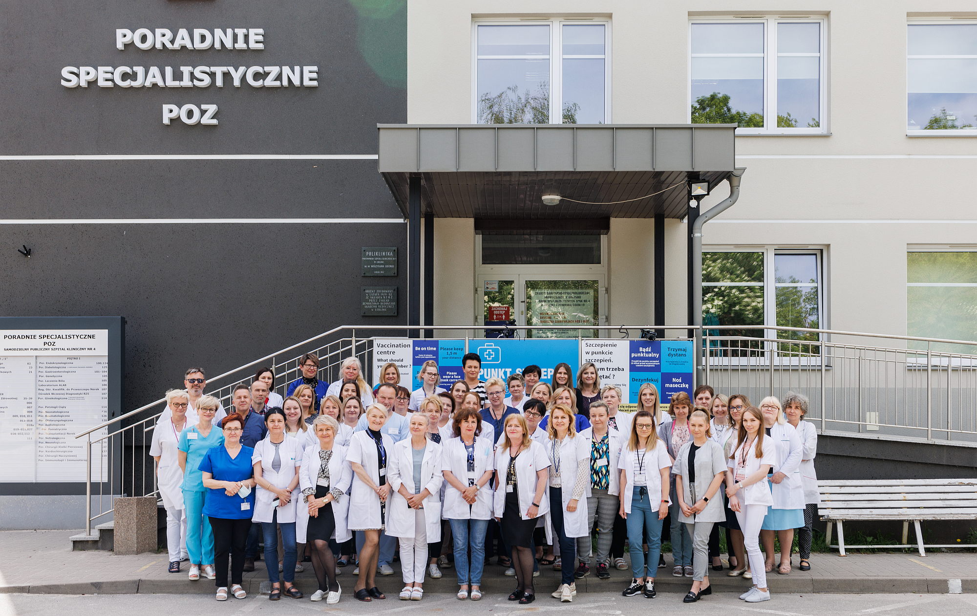 Budynek Poradni Specjalistycznych. Przed wejściem stoją obok siebie pracownicy.  