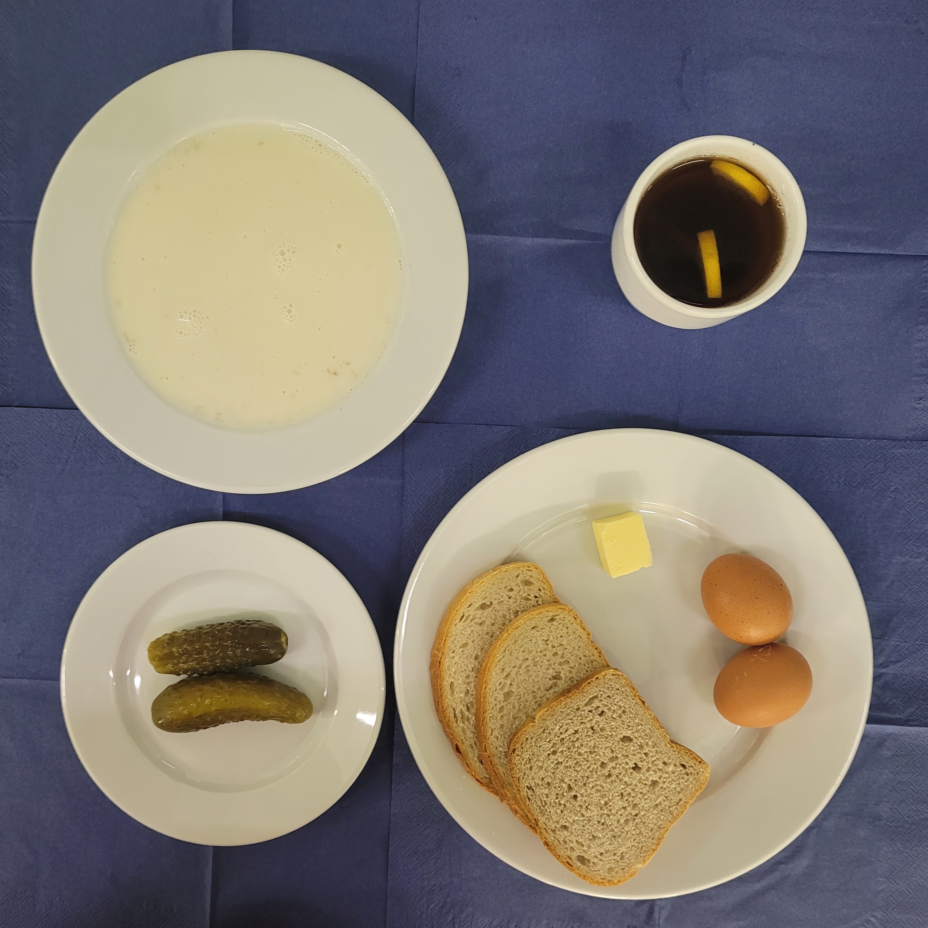 na talerzach płatki owisane na mleku, chleb pszenny, chleb sitkowy, masło, jajko gotowane 2 szt., ogórek kiszony w kubku herbata z cytryną